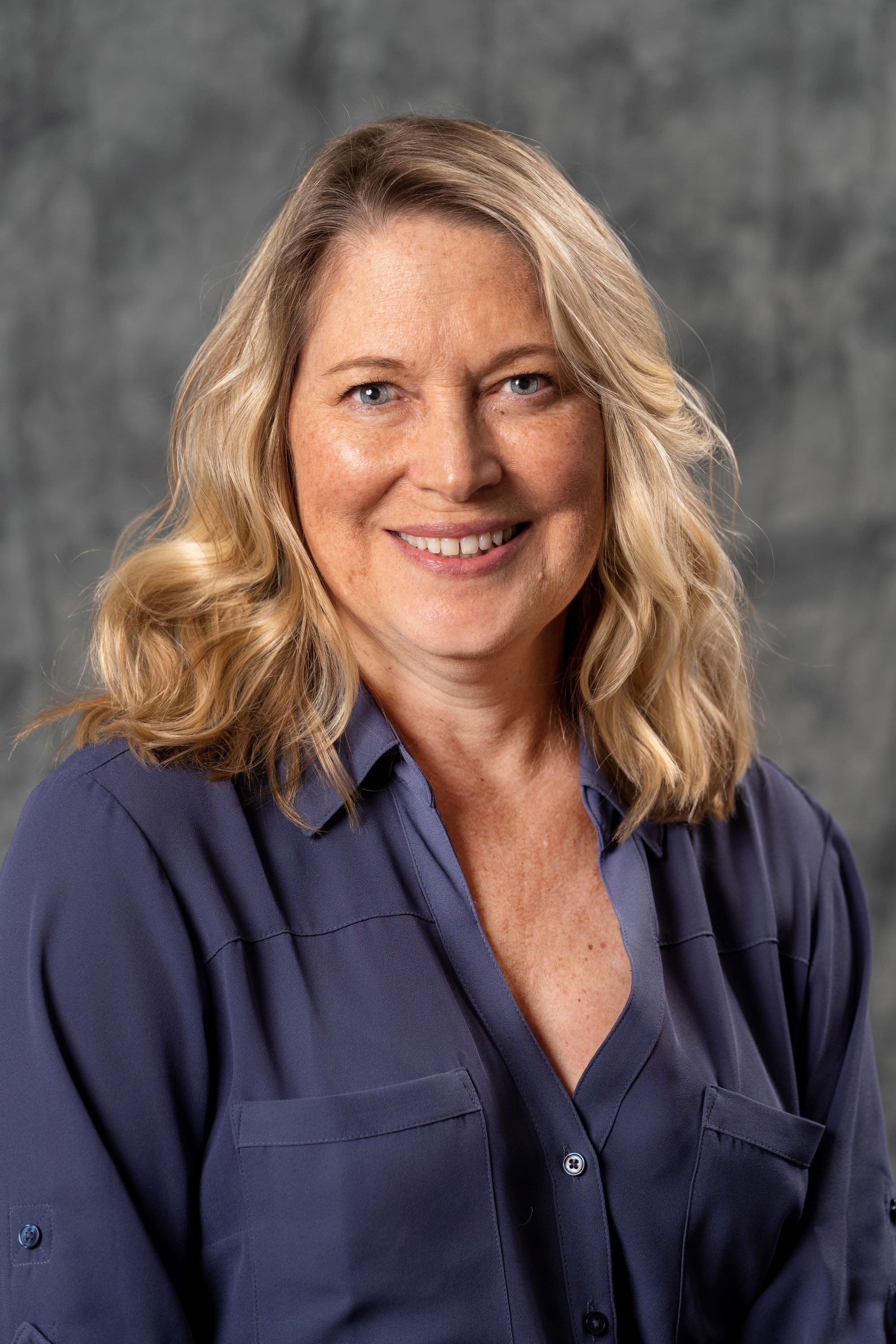 Carol Davies, with wavy shoulder-length blonde hair and wearing a navy blue collared shirt 