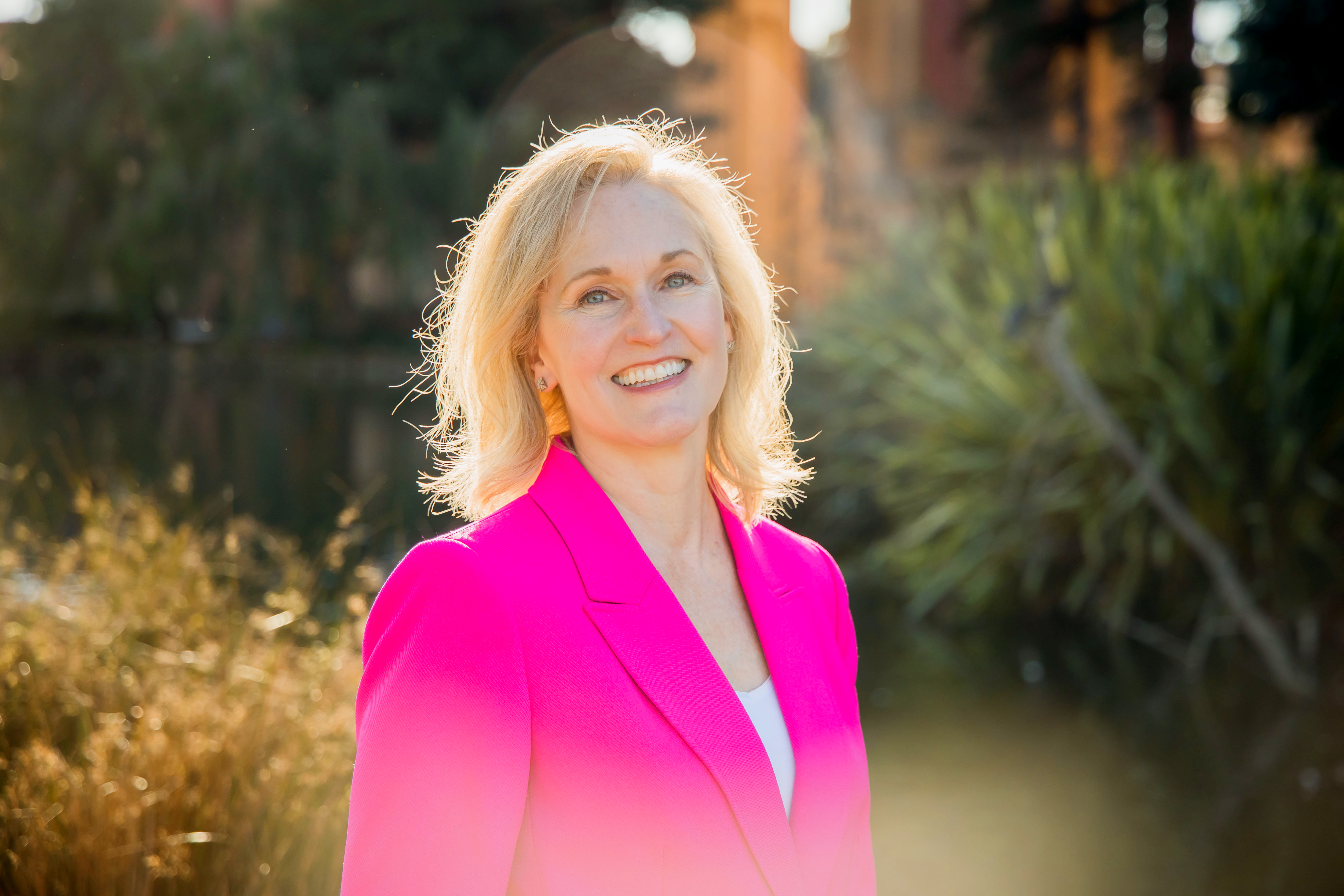 Susan M. Davis Susan M. Davis with blonder hair poses outdoors wearing a fuschia blazer