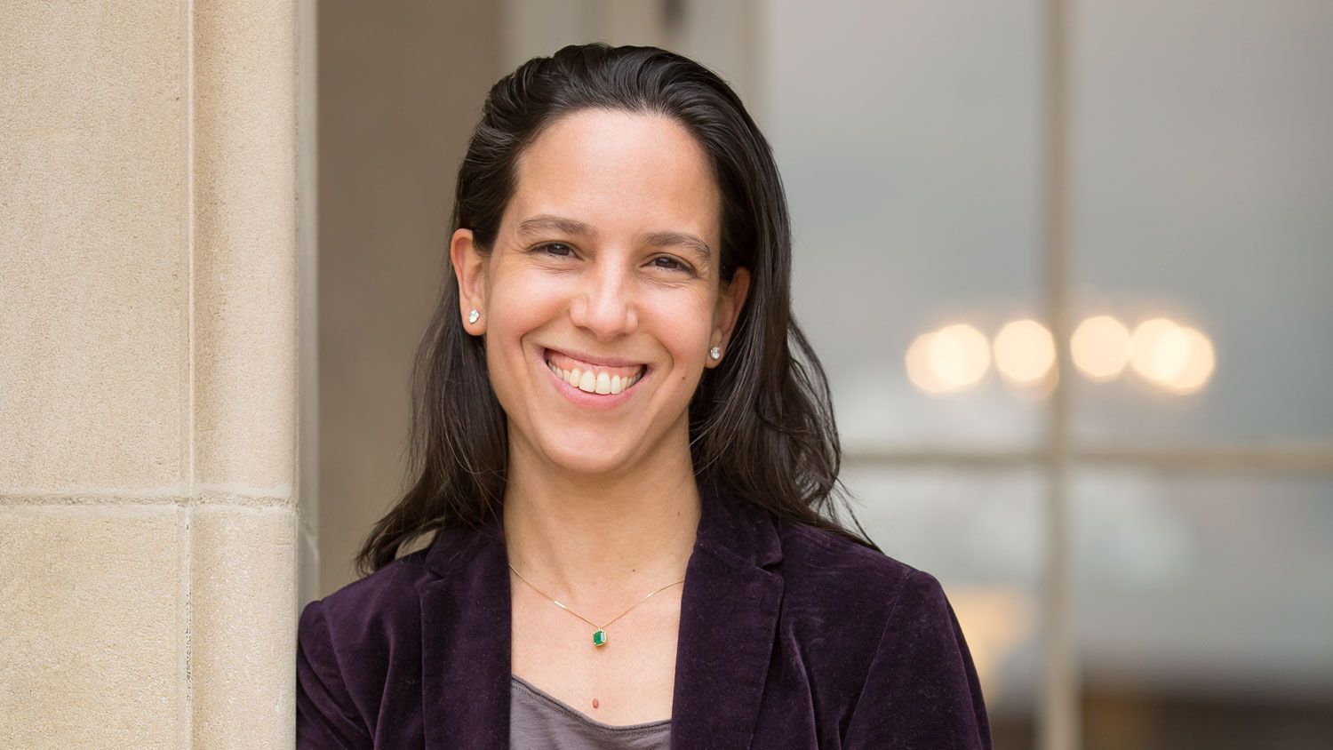Jimena Canales Person with black hair, earings, and an emerald necklace standing and smiling