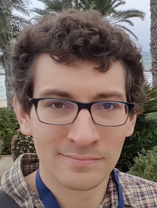 Person wearing glasses and a plaid shirt standing in front of a brick wall with vines.