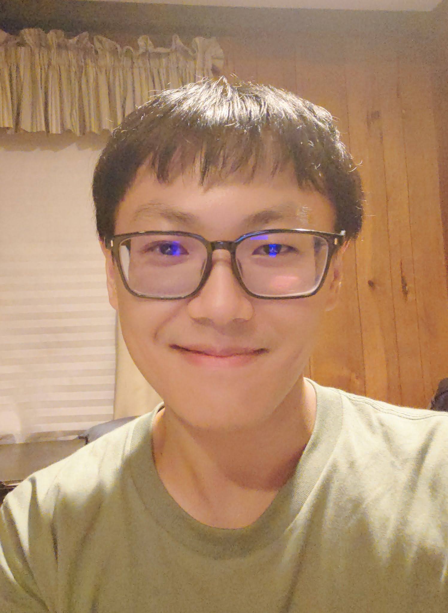 Person with glasses smiling at the camera in a room with a curtained window in the background.