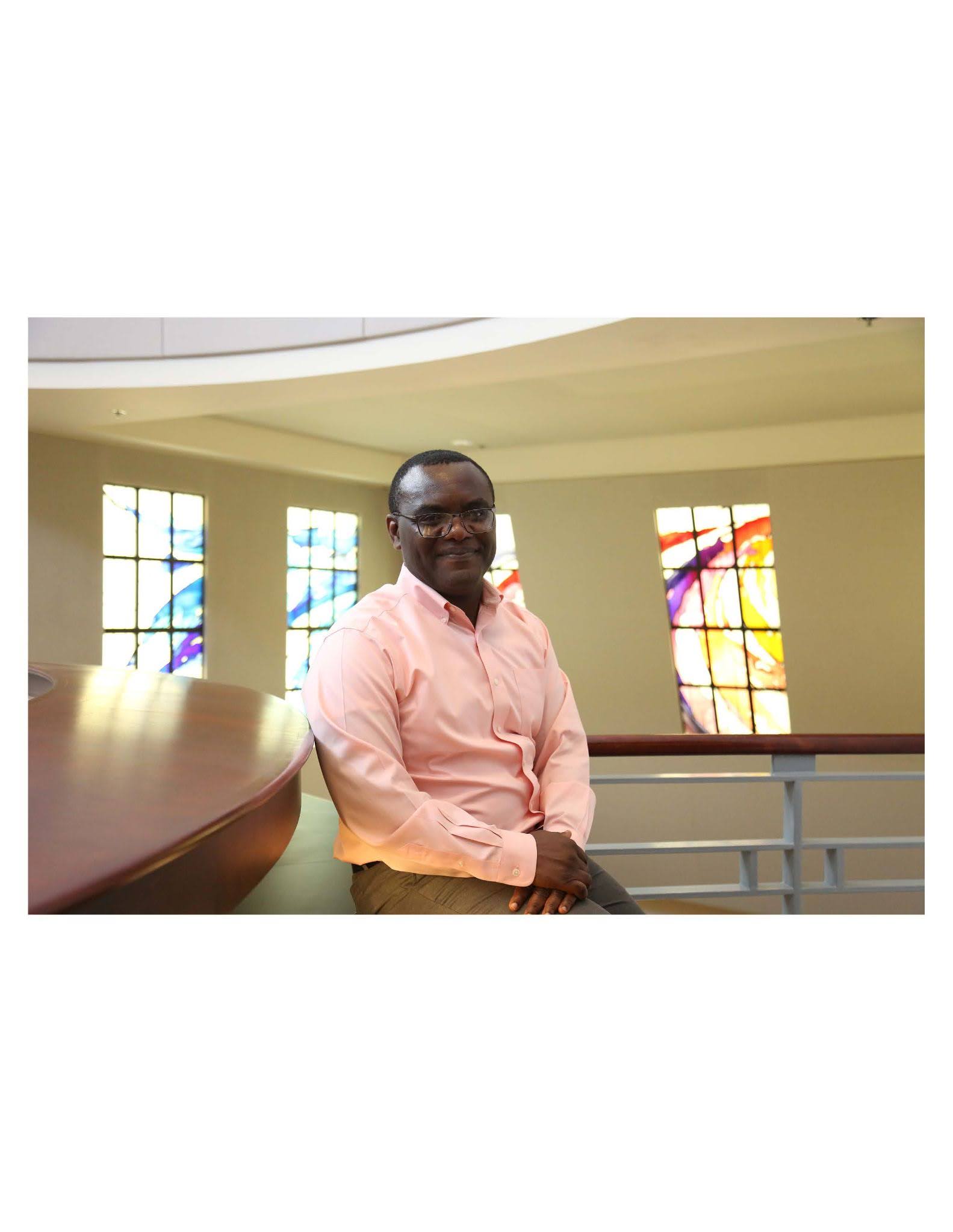 Person sitting on a bench inside a building with large colorful stained glass windows in the background.