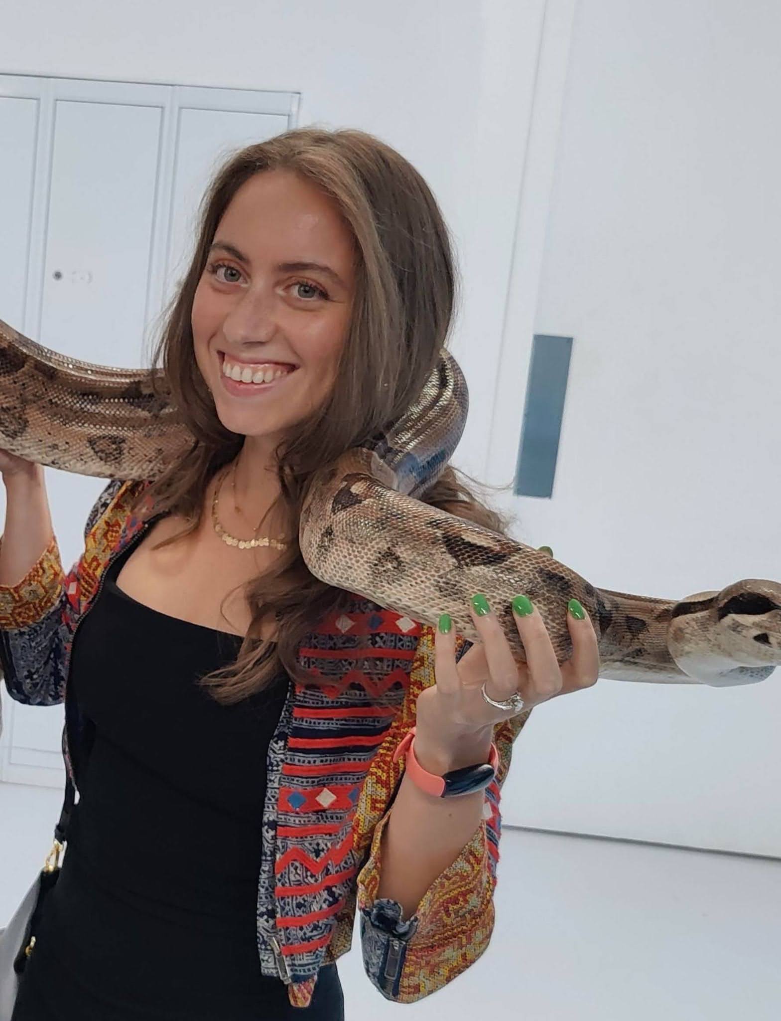 A person smiling while holding a large snake in a room with white walls.