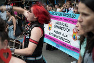 Anti-capitalist protest groups Participants holding a banner at an LGBTIQ+ and student pride march, with various signs and a crowd in the background.