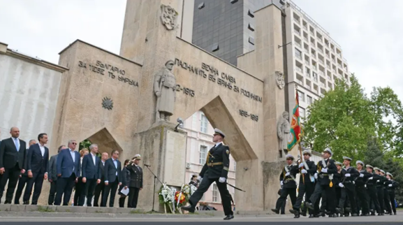Military parade Ceremonial military parade in front of a stone monument, with officials in suits watching. Soldiers in navy uniforms march solemnly, conveying respect.