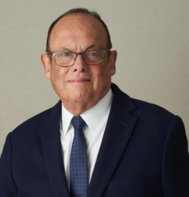 Kingsley Bolton Individual wearing glasses and a dark suit poses in front of a tan background