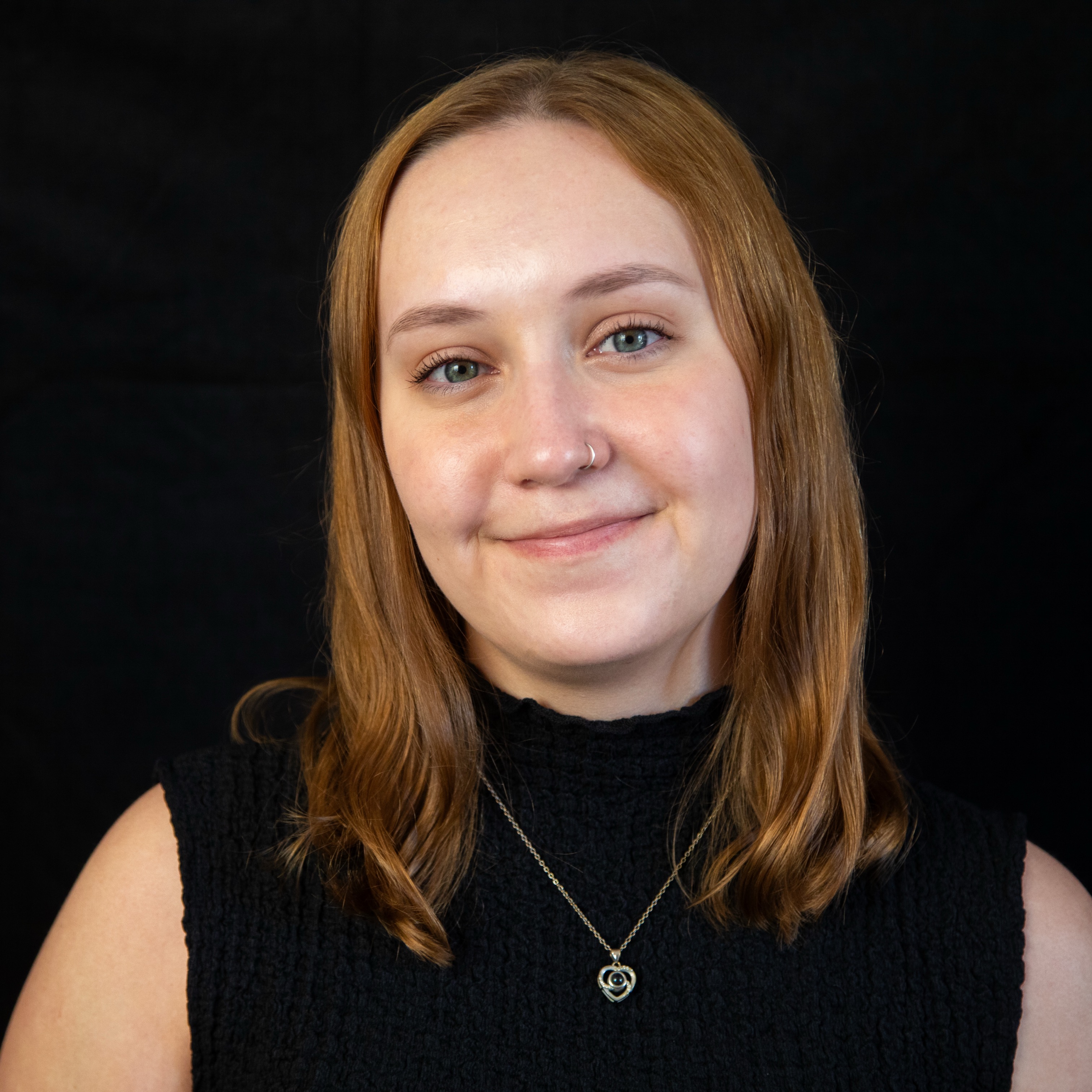 a smiling woman wearing a necklace poses in front of a black backdrop