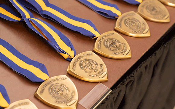 Gold medals with blue and yellow ribbons are neatly arranged on a table. Each medal is inscribed with "Chancellor's Award for Excellence," conveying achievement.