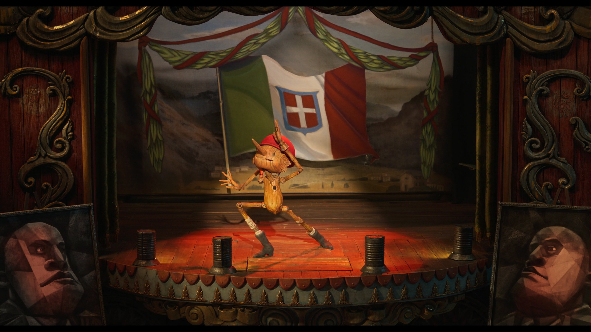 Guillermo del Toro's Pinocchio a screenshot from Guillermo del Toro's Pinocchio; Pinocchio is on a stage with the background being the flag of the kingdom of Italy