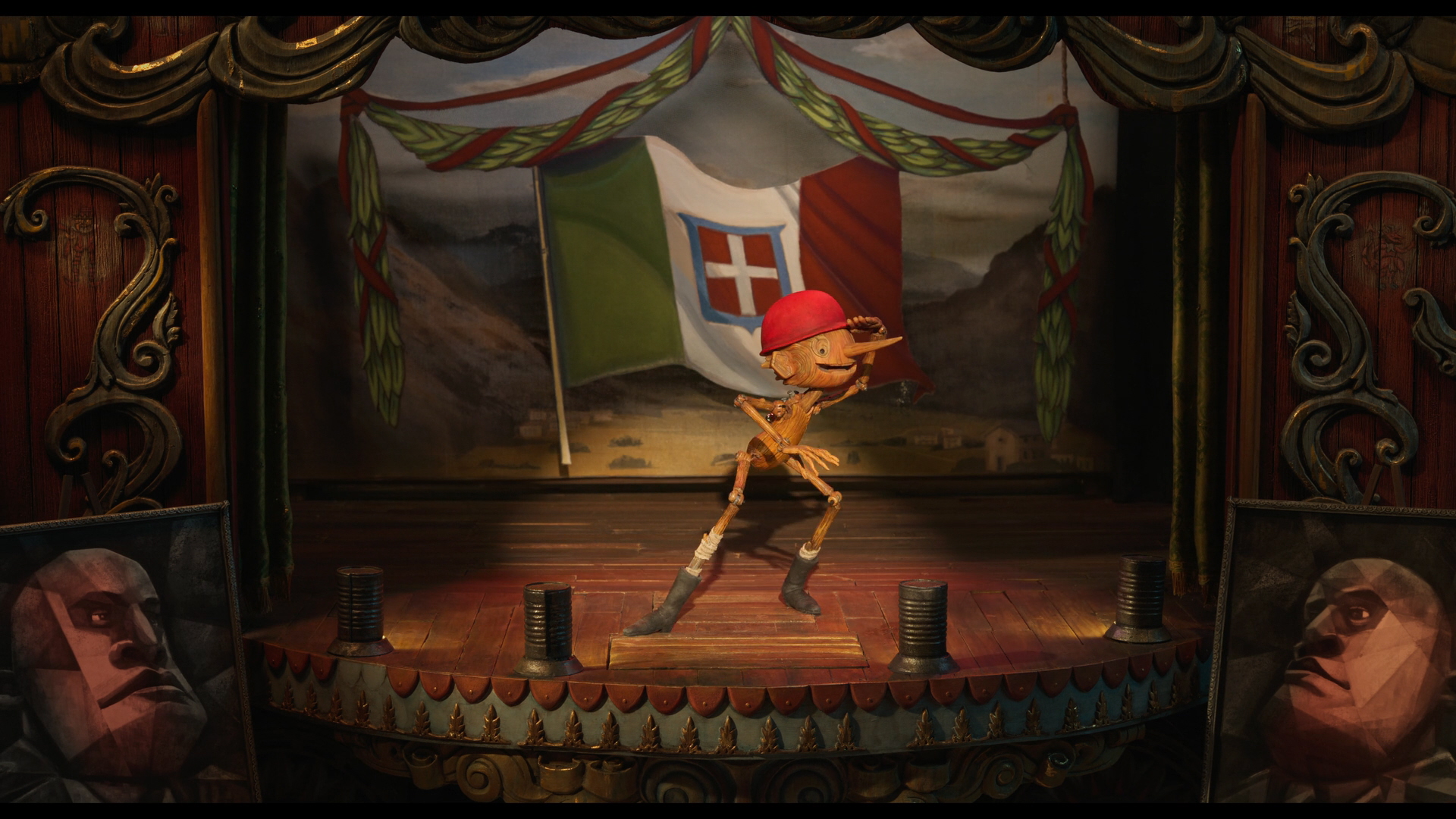 Guillermo del Toro's Pinocchio a screenshot from Guillermo del Toro's Pinocchio; Pinocchio is on a stage with the background being the flag of the kingdom of Italy
